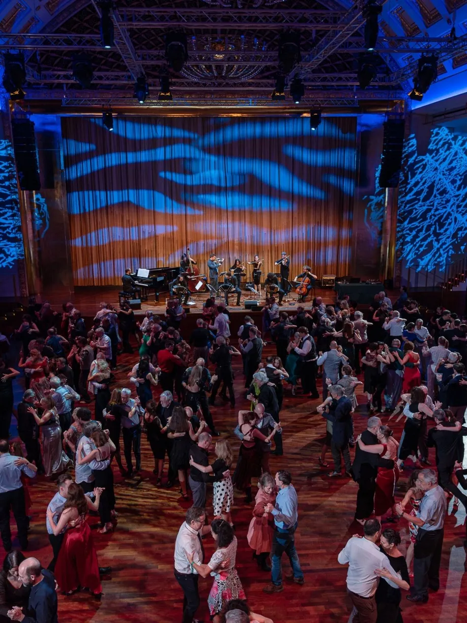 Zahlreiche Paare tanzen Tango im Bénazetsaal des Kurhauses Baden-Baden, während ein Ensemble live auf der Bühne spielt