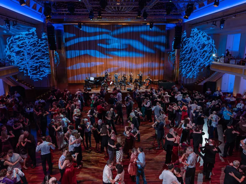 Zahlreiche Paare tanzen Tango im Bénazetsaal des Kurhauses Baden-Baden, während ein Ensemble live auf der Bühne spielt