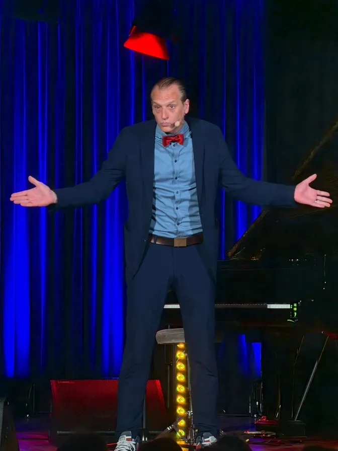 Max Ruhbaum mit roter Fliege und Headset auf der Bühne bei Comedy im Kurhaus Baden-Baden