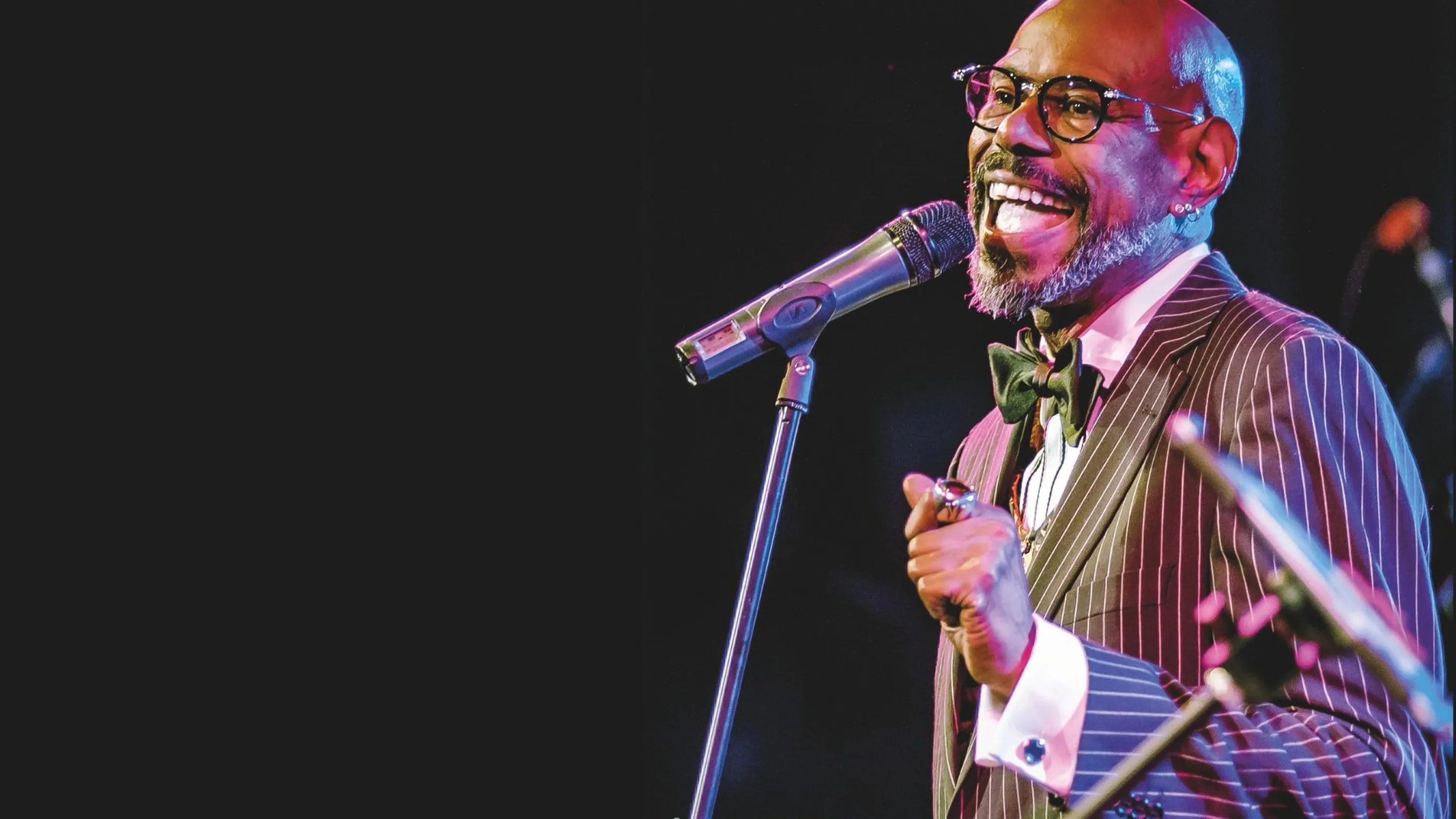 Dennis LeGree singt im Anzug mit Fliege und Brille an einem Mikrofon auf der Bühne